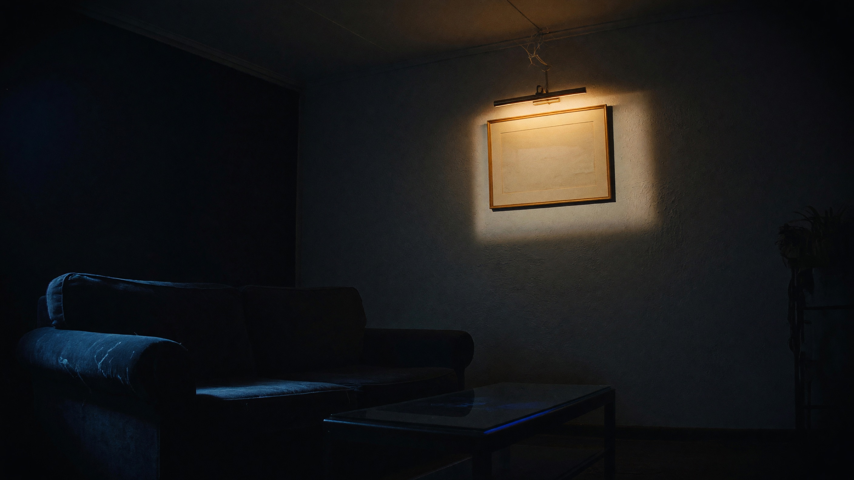 A dark living room with one warmly lit picture on the wall